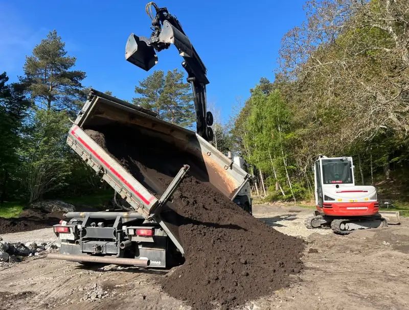 Lastbil tippar jord med grävmaskin i bakgrunden